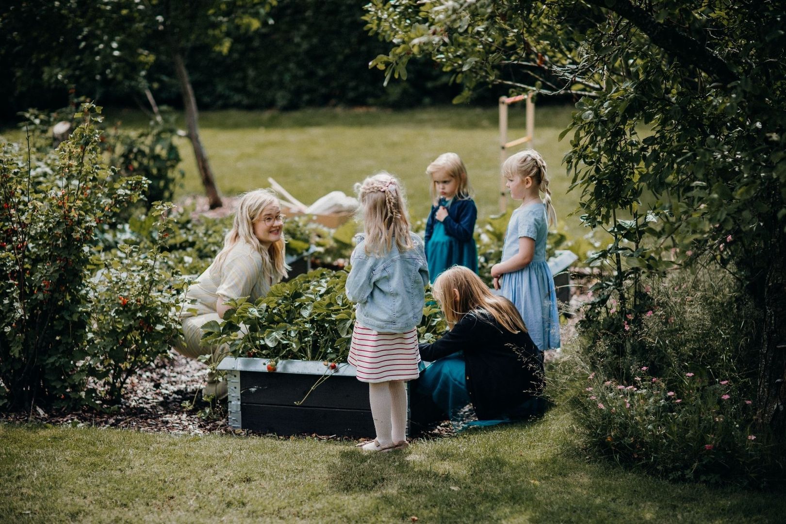 Vuxen och barn samlas i en trädgård vid en förskoleliknande miljö